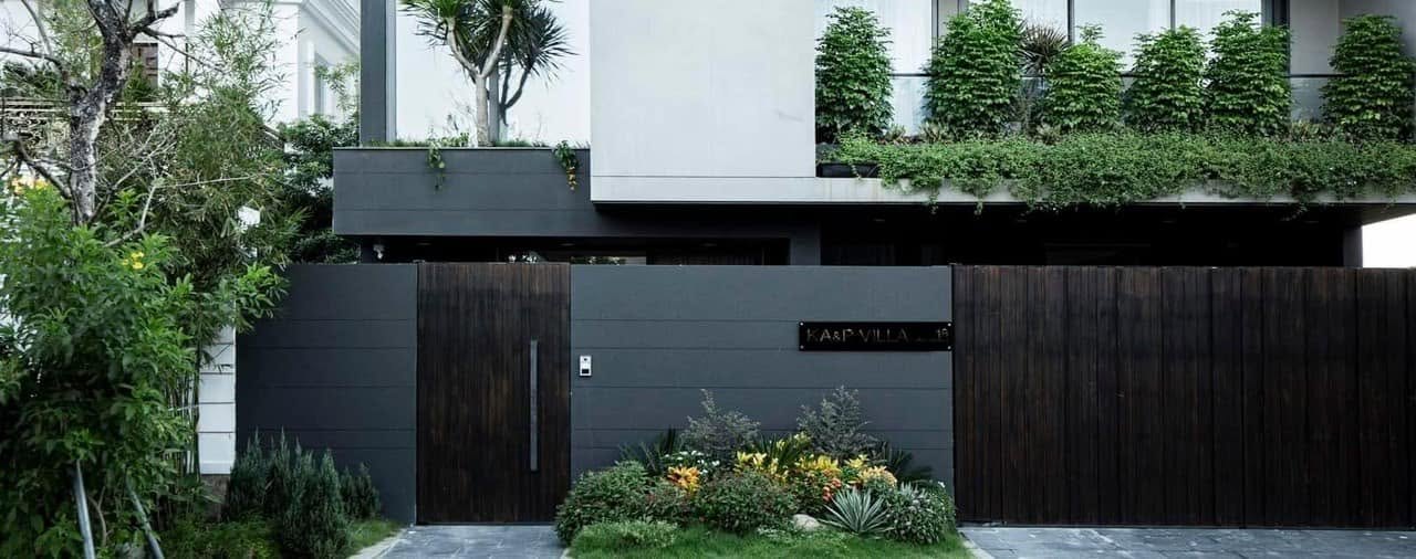 Mặt tiền KA&P Villa: cổng gỗ, tường xám đen và cây xanh